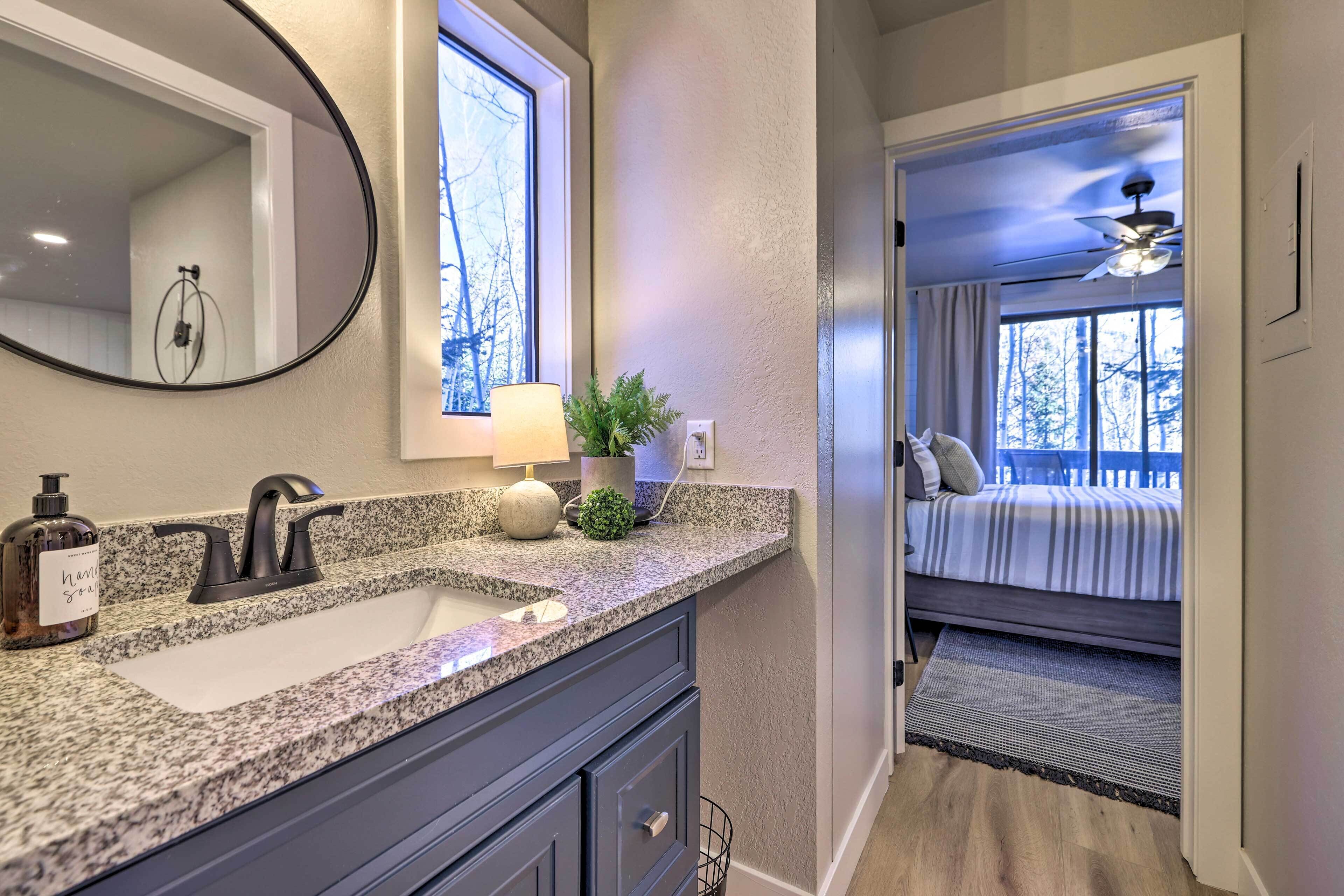 A bathroom with a granite countertop, a large mirror, a sink, and a window.