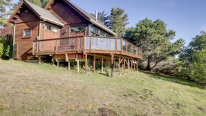 Eine Holzhütte mit einer Terrasse, umgeben von Bäumen und Gras.