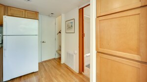 Una cocina con armarios de madera, un refrigerador blanco y una puerta que da a un pasillo.