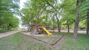 Un parque infantil con tobogán y estructuras para escalar, rodeado de árboles.