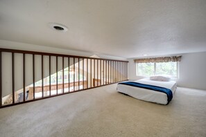 Une chambre à coucher avec un lit, une fenêtre avec des rideaux, une bouche d’aération au plafond et une vue sur un escalier.