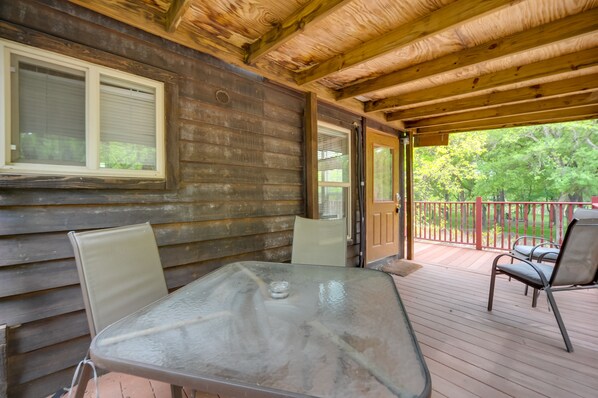 Une terrasse en bois avec une table et des chaises en verre, une rambarde en bois et une vue sur la verdure.