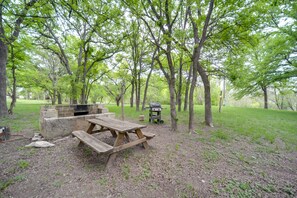 Un área de picnic con una mesa y bancos de madera, una parrilla y un hogar para fuego de ladrillo.