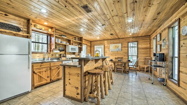 Het interieur van een houten chalet met een keuken, inclusief een koelkast, houten keukenkastjes, een barkruk en een eettafel.