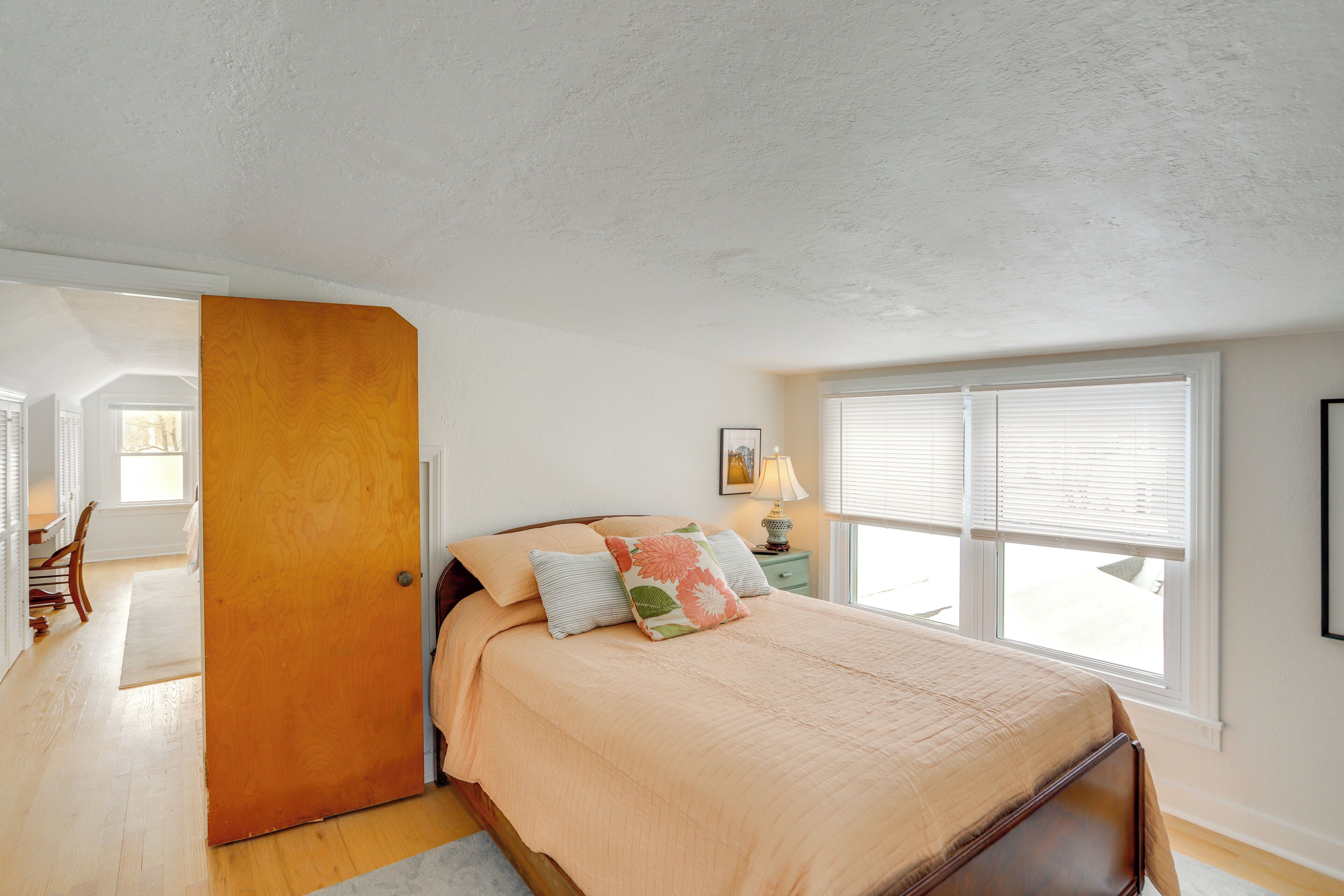 A bedroom with a bed, a nightstand, a lamp, and a window with blinds.