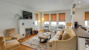 A living room with a fireplace, a sofa, a coffee table, and a TV mounted on the wall. - Cozy Cottage in Historic Village: Near Cedar Point (Milan)