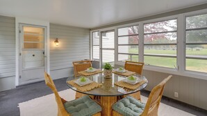 A dining area with a glass table surrounded by wicker chairs, a white door, and large windows offering a view of the outdoors. - Cozy Cottage in Historic Village: Near Cedar Point (Milan)