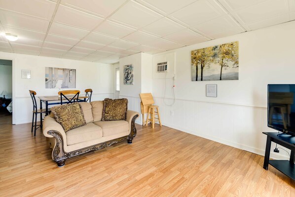 Un salon avec un canapé beige, un plancher en bois et des œuvres d’art accrochées aux murs.