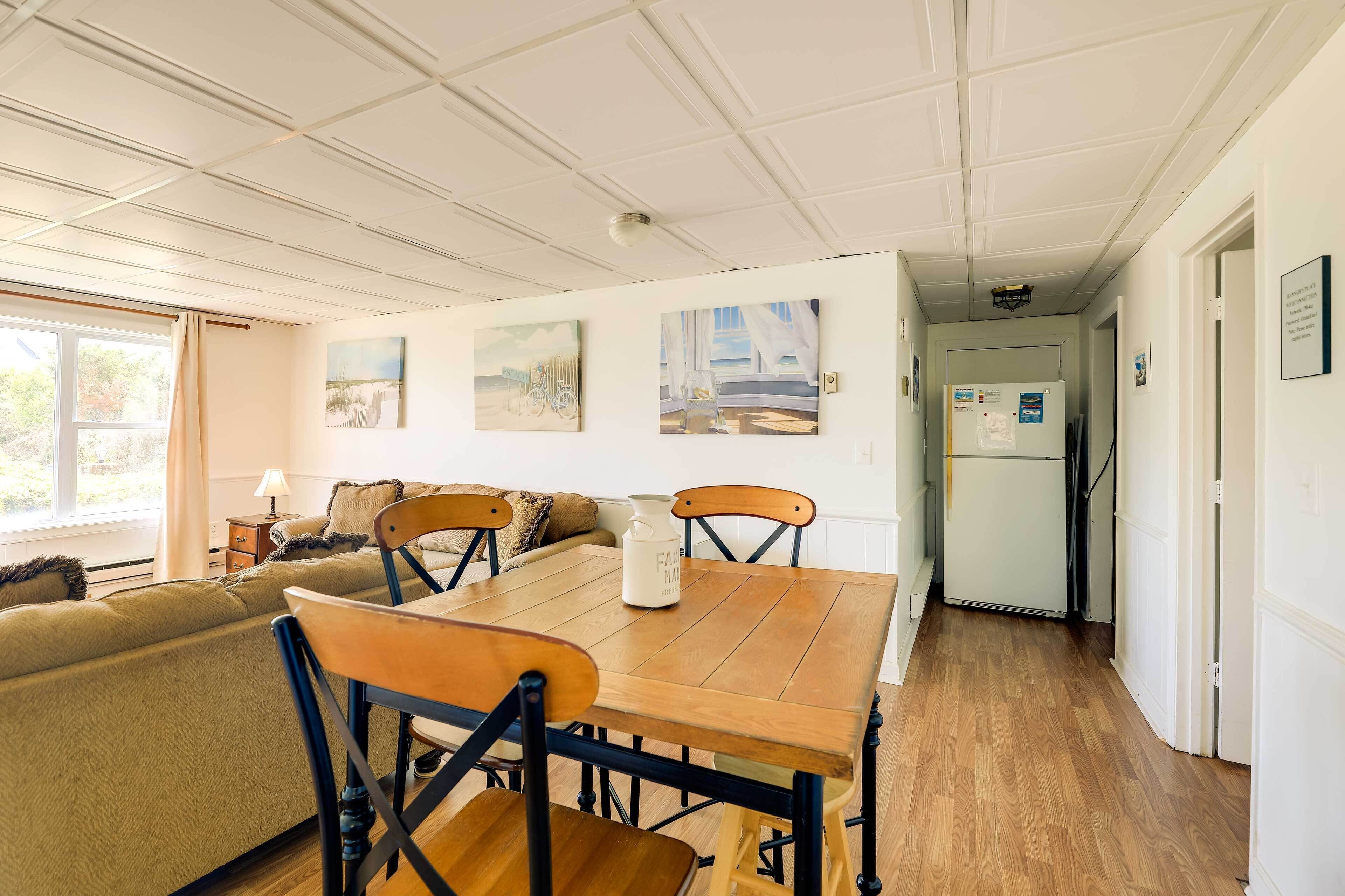 Una habitación acogedora con una mesa de comedor de madera, un sofá y una cama. Hay pinturas en la pared y un refrigerador en la esquina.