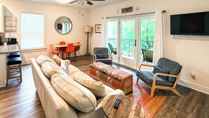 A living room with a sofa, ottomans, a coffee table, a TV, a dining area with chairs, and a balcony with a view. - 'salt & Serenity on 30a' Walk to Santa Rosa Beach! (Santa Rosa Beach)