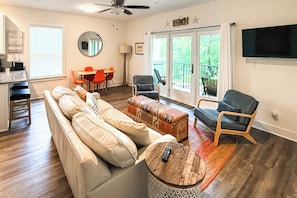 A living room with a sofa, ottomans, a coffee table, a TV, a dining area with chairs, a balcony, and a ceiling fan. - 'salt & Serenity on 30a' Walk to Santa Rosa Beach! (Santa Rosa Beach)