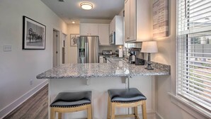 A modern kitchen with white cabinets, a stainless steel refrigerator, granite countertops, and two bar stools. - 'salt & Serenity on 30a' Walk to Santa Rosa Beach! (Santa Rosa Beach)