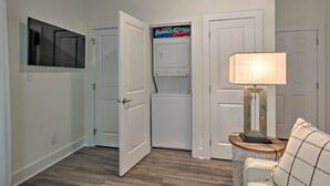 A laundry room with a washing machine and dryer, a chair with a lamp, and a television mounted on the wall. - 'salt & Serenity on 30a' Walk to Santa Rosa Beach! (Santa Rosa Beach)