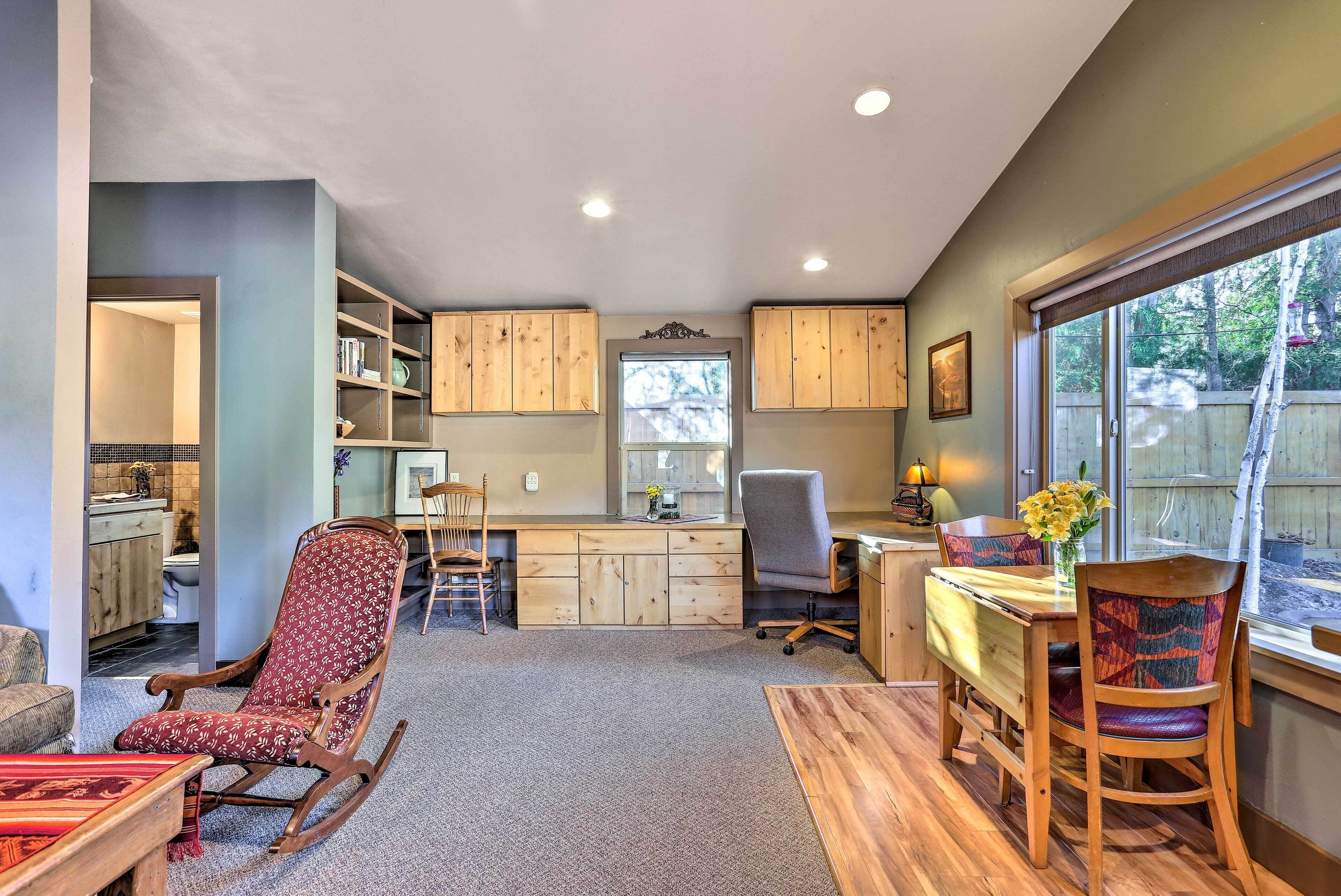 A cozy living room with a rocking chair, a dining table with chairs, and a kitchen area with wooden cabinets and a window.