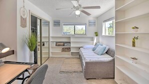 Une pièce de taille modeste, dotée d’un ventilateur de plafond, d’un canapé, d’un bureau et d’étagères.