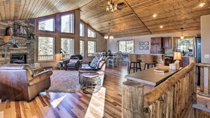 A spacious living area with a fireplace, leather sofa, and a dining area with a wooden table and chairs. - Fairplay Cabin w/ Wraparound Deck & Mountain Views (Fairplay)