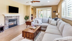 A living room with a stone fireplace, a large sectional sofa, a wooden coffee table, and a ceiling fan.