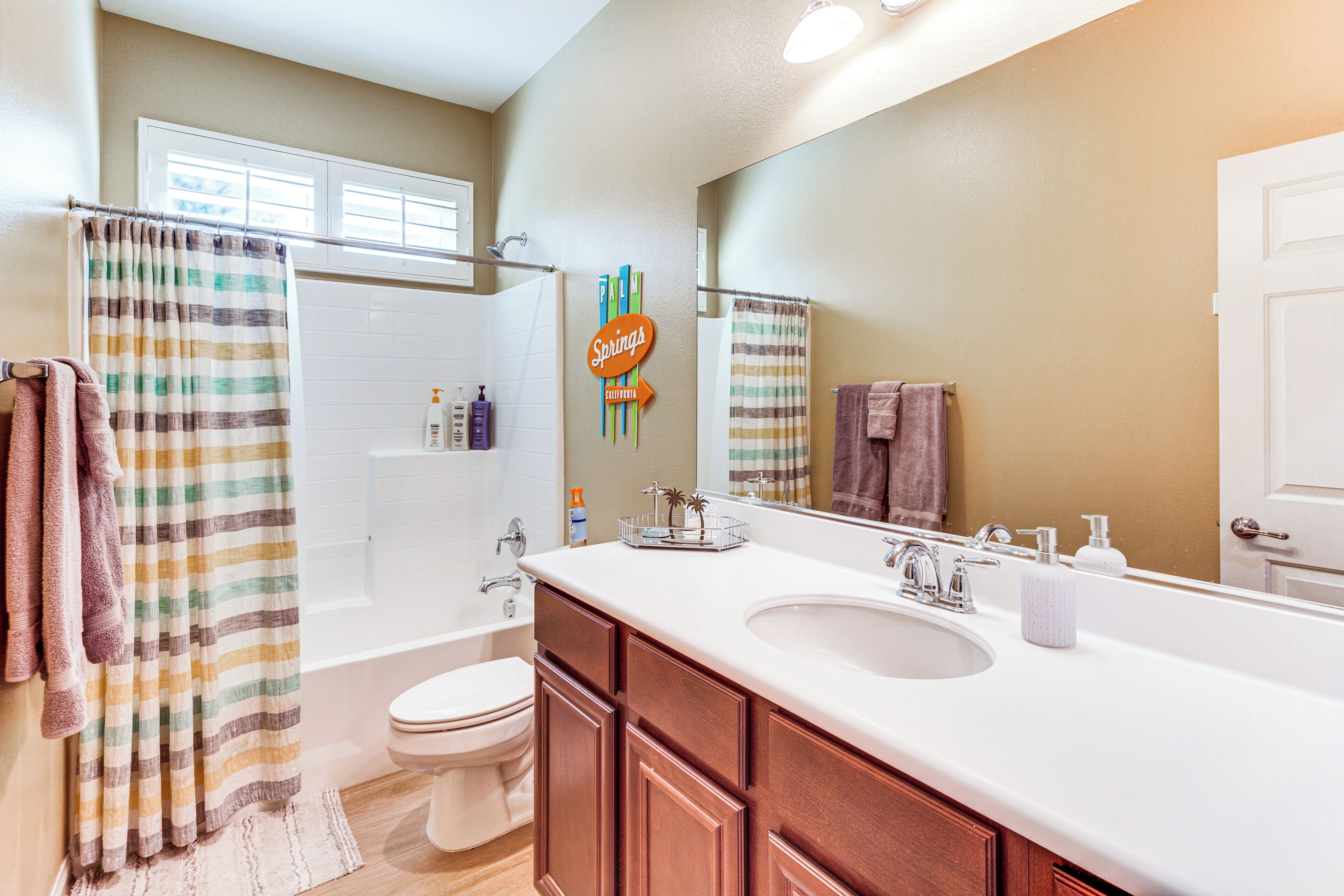 A bathroom with a large mirror, a bathtub, and a toilet. There are towels hanging on the wall and a shower curtain.