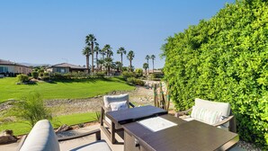 A patio with outdoor furniture, a water feature, and a view of a well-maintained lawn and palm trees.