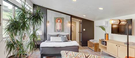 Une chambre à coucher moderne avec un grand lit, une plante en pot, un fauteuil à motifs, un téléviseur et une armoire en bois.