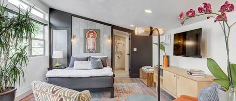A modern bedroom with a bed, a sofa, a TV, and a potted plant.