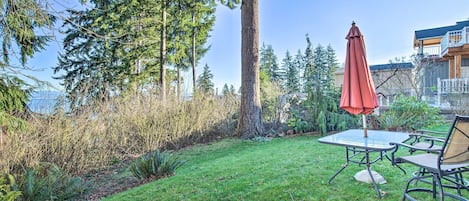 A patio with a table and chairs, surrounded by a grassy area and tall trees.