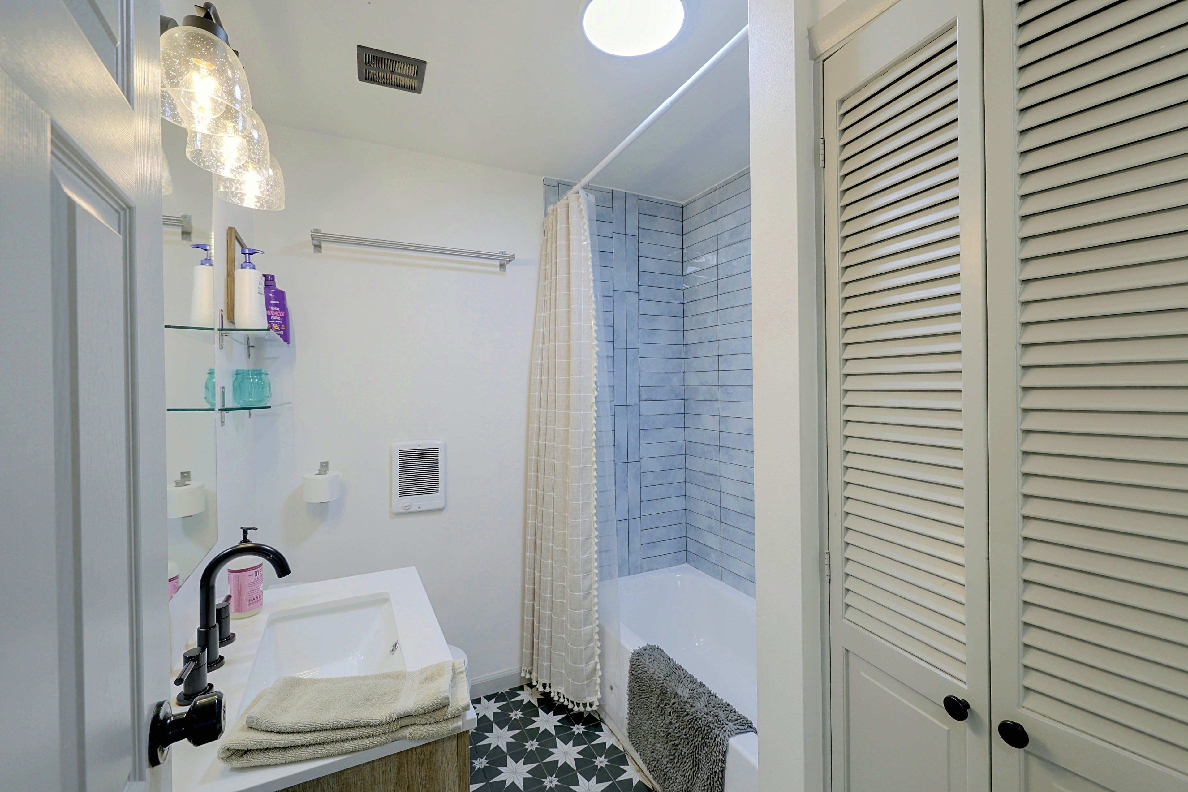 A bathroom with a sink, mirror, shower curtain, and a towel rack.