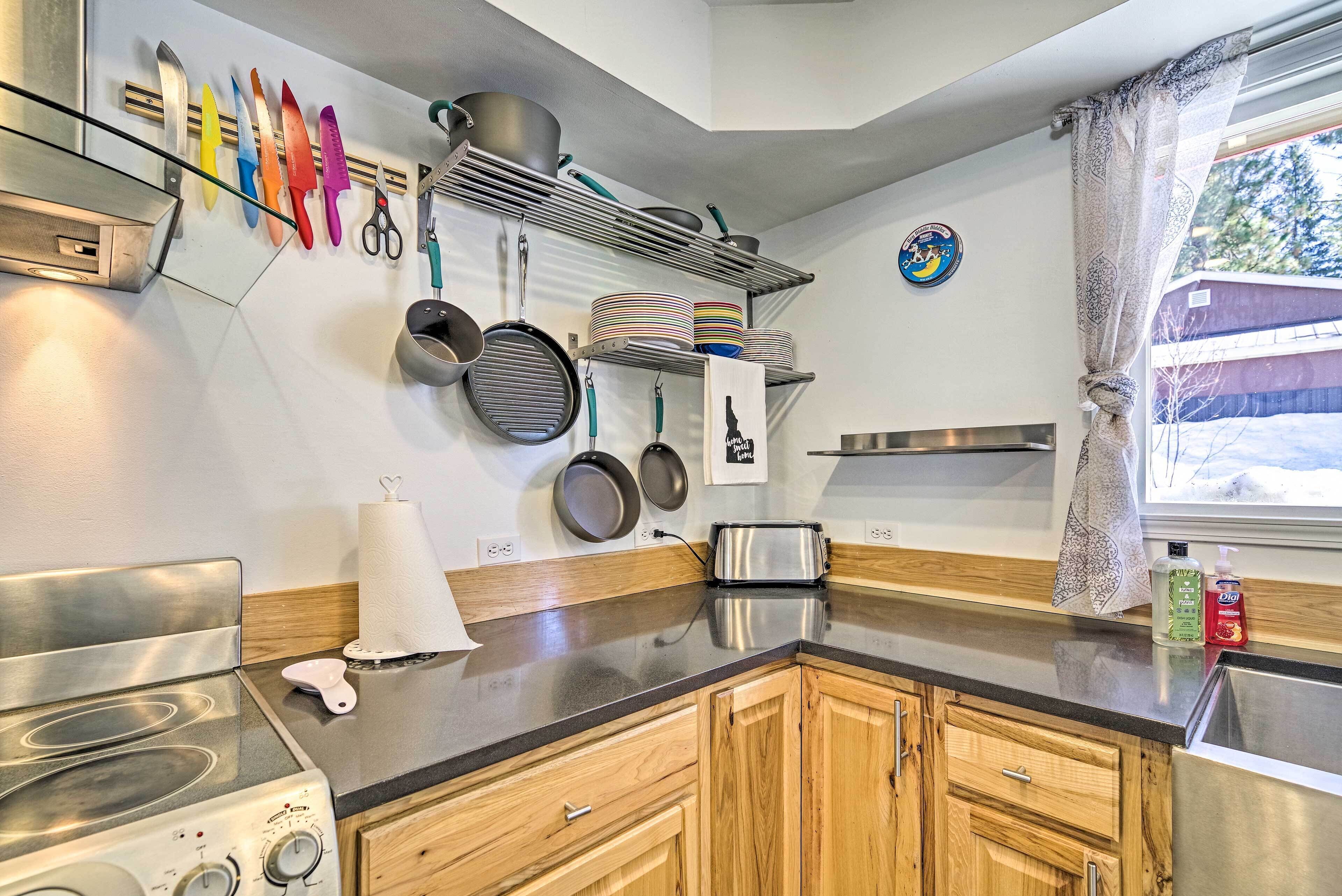 A modern kitchen with wooden cabinets, a stainless steel stove, and a variety of cookware and utensils displayed on the wall.