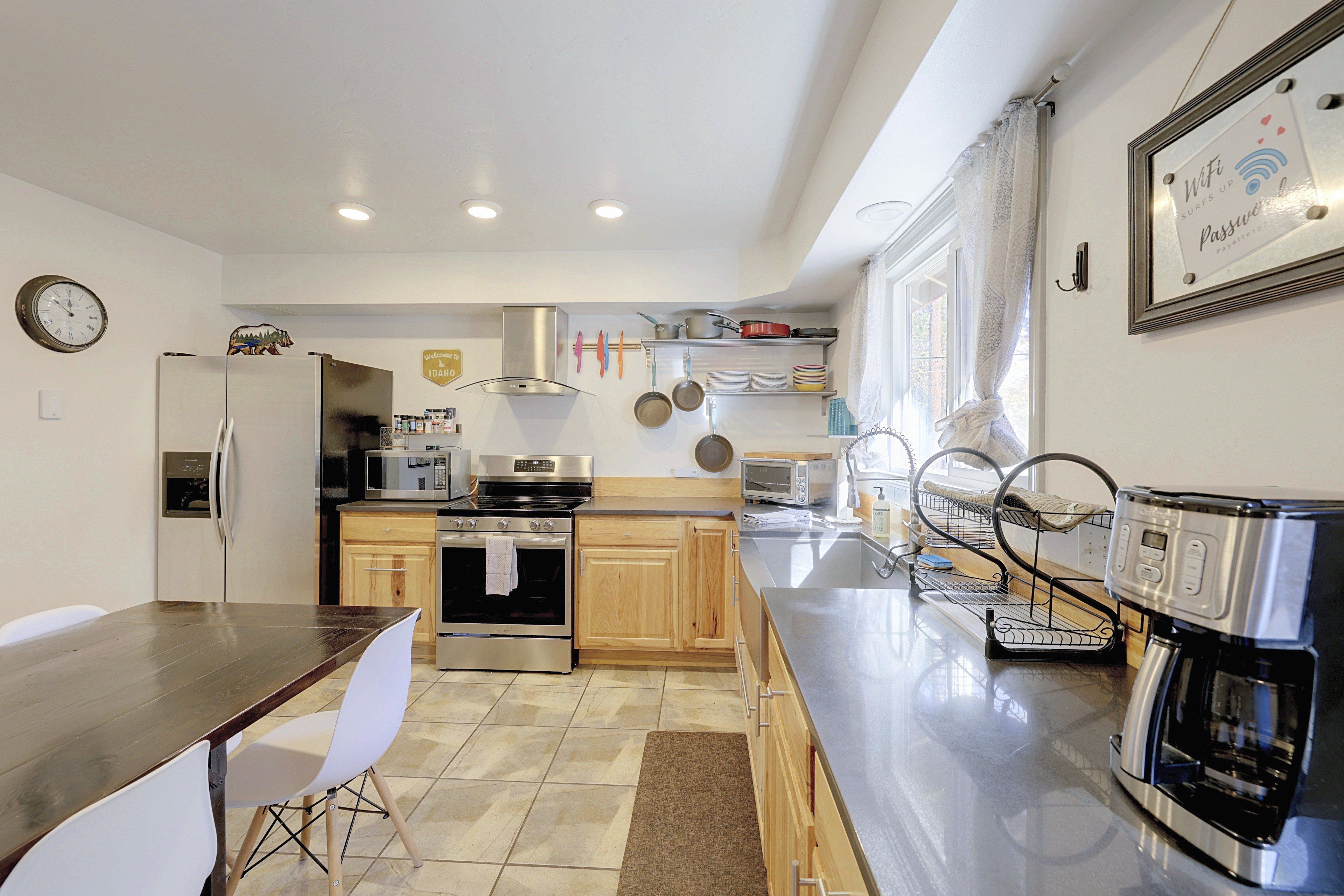 A modern kitchen with stainless steel appliances, a dining area with a wooden table and white chairs, and a large window with curtains.