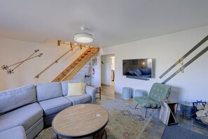 Ein modernes Wohnzimmer mit einem grauen Sofa, einem runden Holztisch, einem grünen Sessel und einem an der Wand befestigten Fernseher.