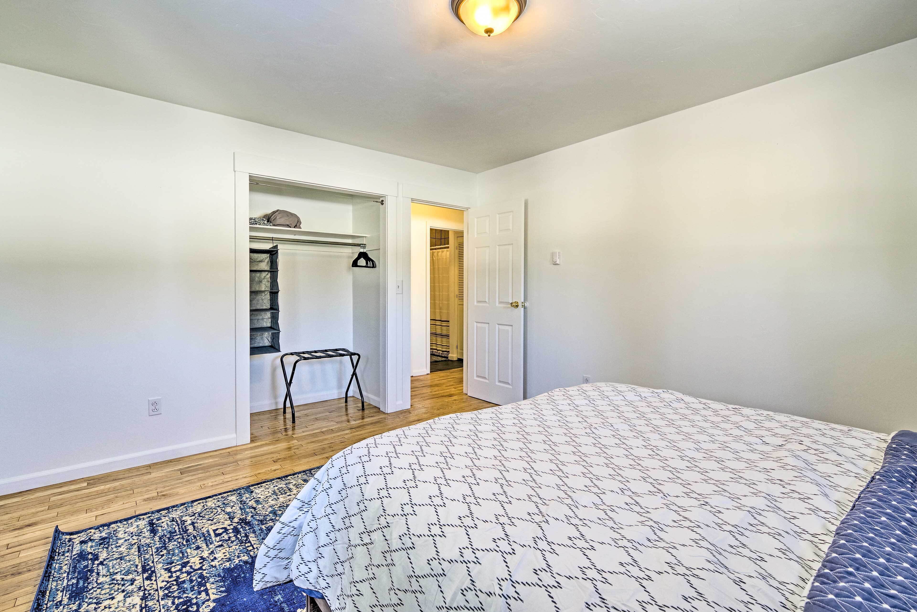 A bedroom with a bed, a blue patterned rug, a white wall, and a wooden floor.