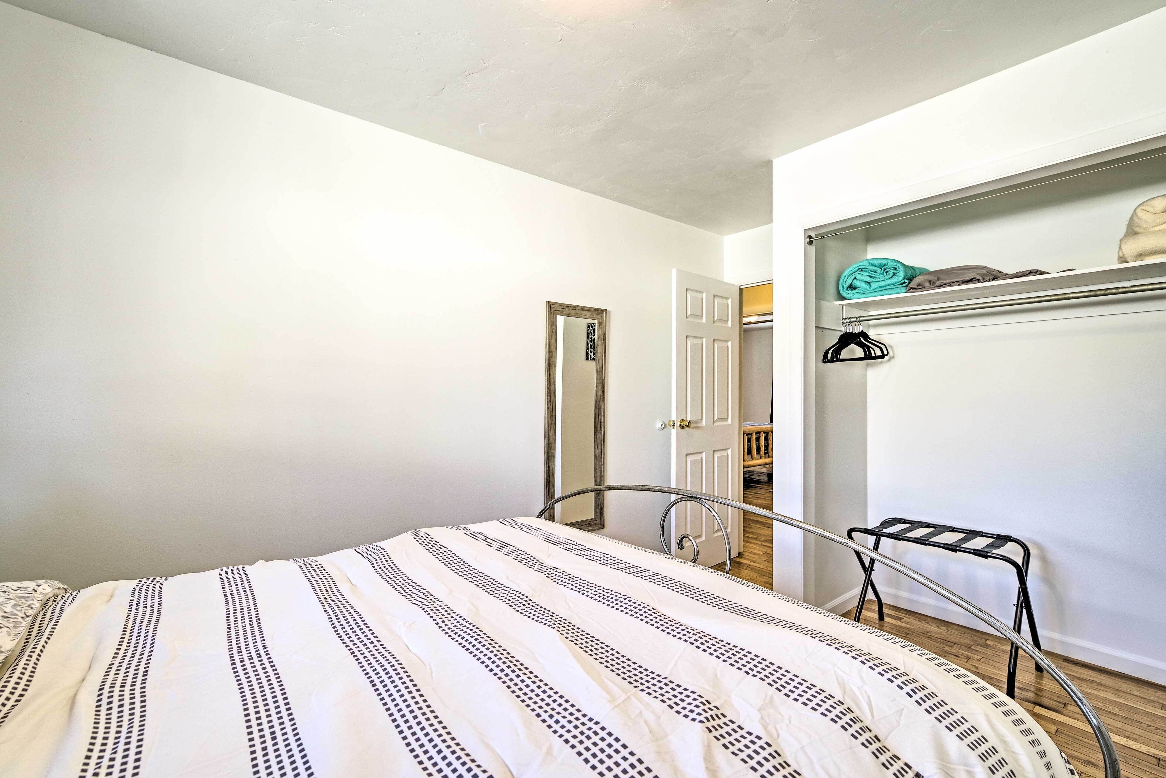 Une chambre à coucher comprenant un lit, un étendoir métallique, une armoire et une porte donnant sur une autre pièce.