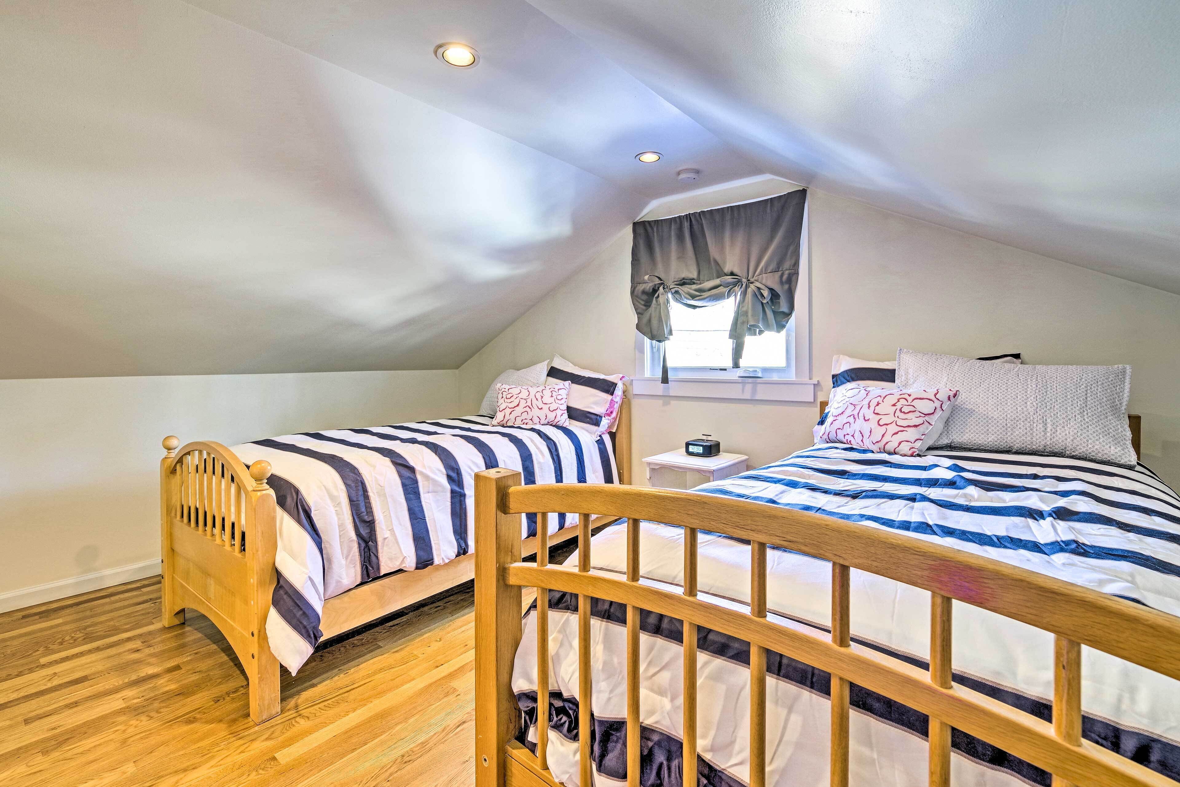 A small, cozy attic bedroom with two wooden beds, a window with curtains, and a small bedside table.