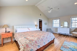 A bedroom with a large bed, a nightstand, a dresser, a mirror, and a ceiling fan.