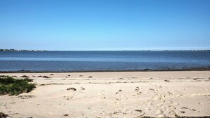A beach with clear blue water and a sandy shore. - Luxe Waterfront East Quogue Home w/ Beach On-site! (East Quogue)