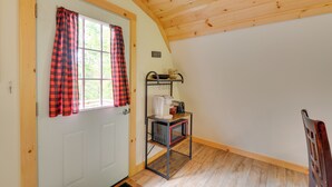 A room with a white door, red and black checkered curtains, a wooden ceiling, a small metal shelf with a microwave, and a sign that says "MAINE". - Pet-friendly Prospect Apartment: 7 Mi to Beach! (Stockton Springs)