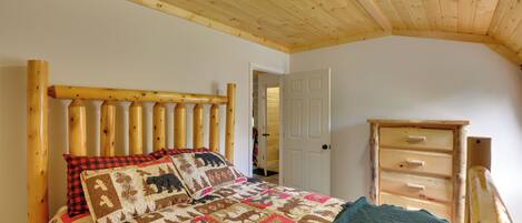 A bedroom with a wooden headboard, a quilted bedspread, a wooden dresser, and a door leading to another room.