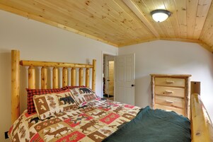 Un dormitorio con cabecera de madera, colcha acolchada, cómoda de madera y una puerta que da a otra habitación.