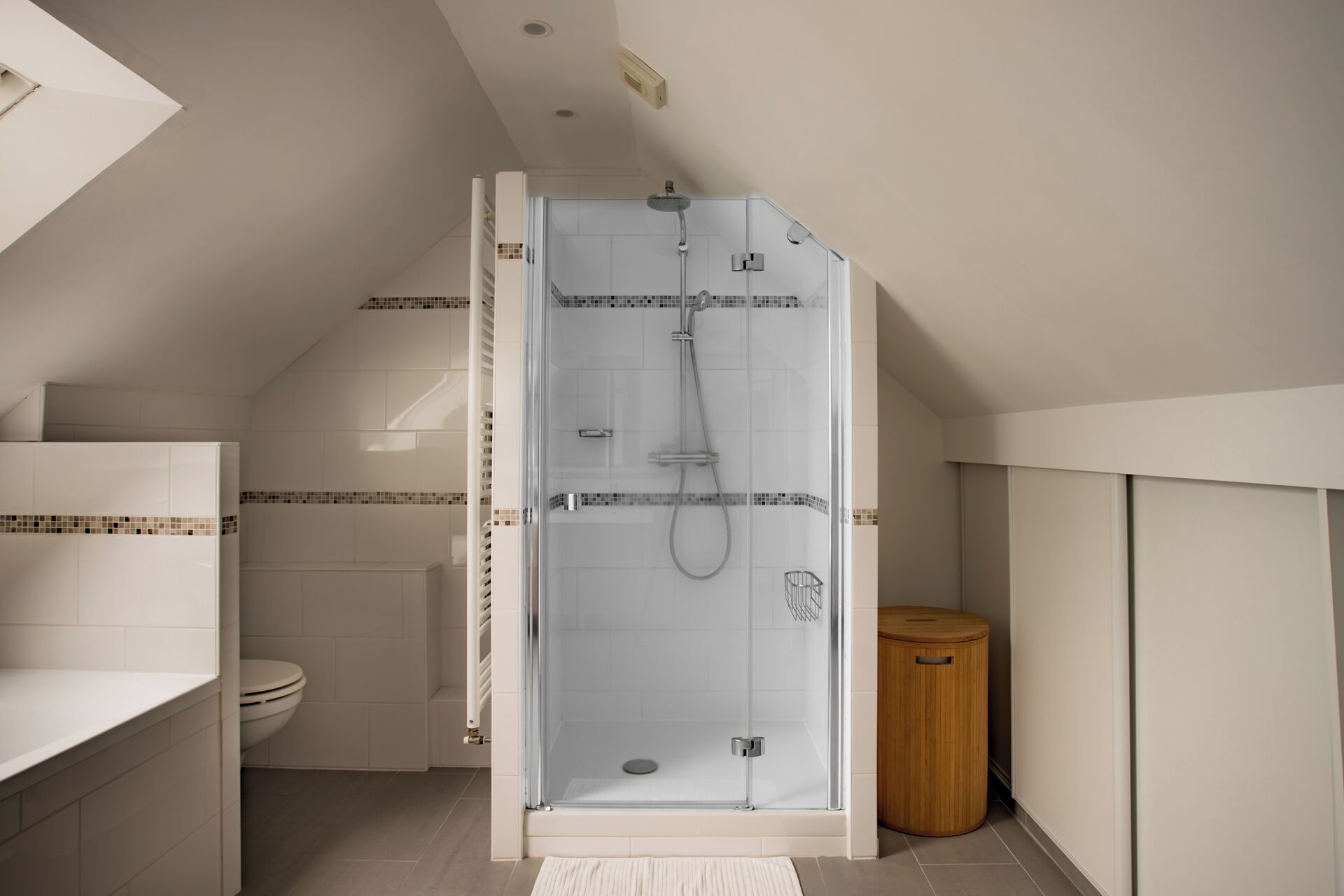 A modern bathroom with a glass-enclosed shower, a toilet, and a wooden waste bin.