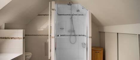 A modern bathroom with a glass-enclosed shower, a toilet, and a wooden waste bin.