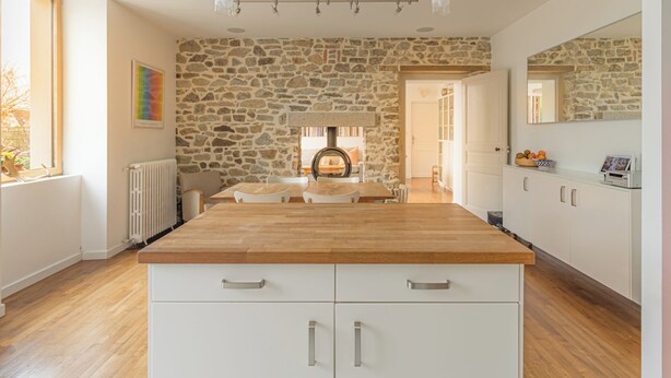 Une cuisine moderne avec un mur de crédence en pierre, un plan de travail en bois et des meubles de cuisine blancs.