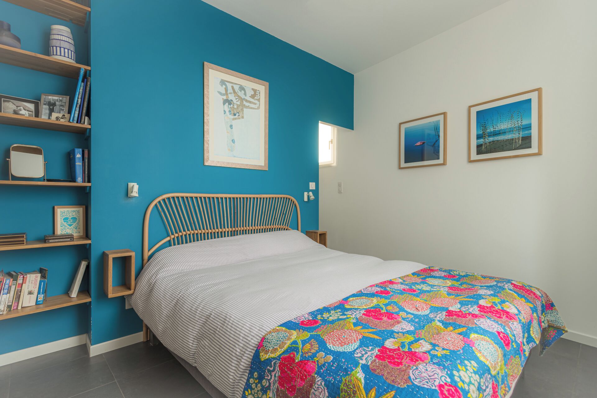 A bedroom with a bed, a blue wall, a wooden headboard, and a bookshelf.