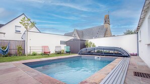 Une piscine entourée d’une terrasse en pierre et protégée par une paroi en verre.