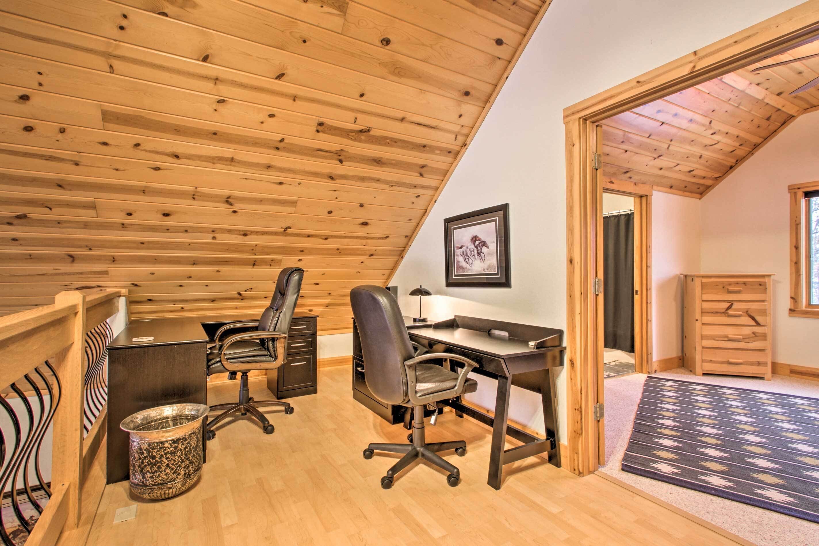 A loft bedroom with a sloped ceiling, wooden floor, a desk with a chair, a bed, a small cabinet, and a framed picture on the wall.
