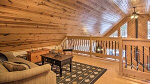 A cozy loft bedroom with a wooden ceiling, a wooden staircase, a sofa, a small table, and a view of the outdoors.