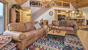 A spacious living room with two leather sofas, a wooden coffee table, and a colorful rug. A wooden staircase leads to an upper level.