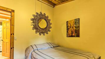 A bedroom with a bed, a mirror, and a painting on the wall.