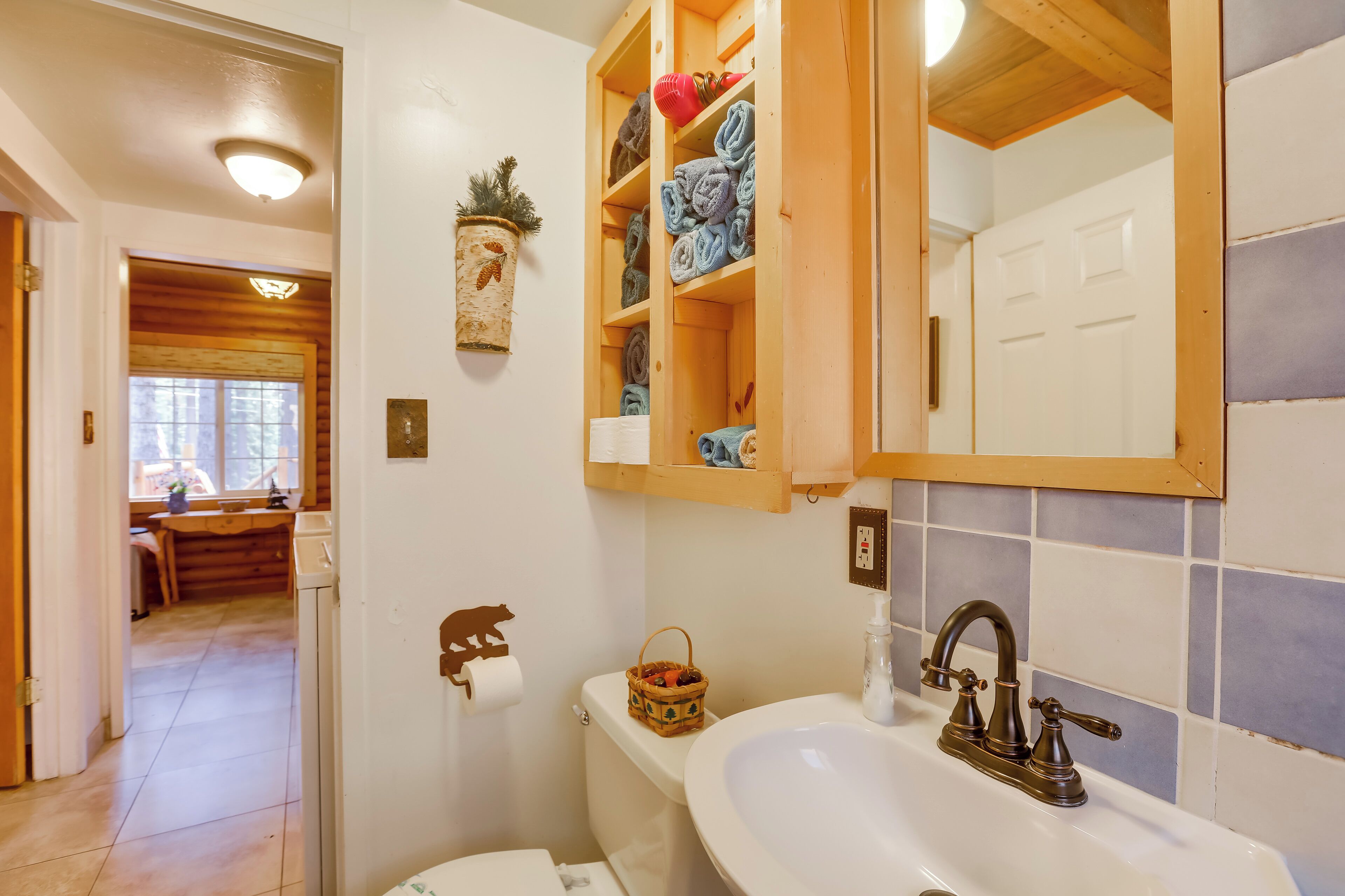 A bathroom with a wooden vanity, a sink, and a toilet. There is a window with a view of the outside, and a wooden cabinet above the sink.