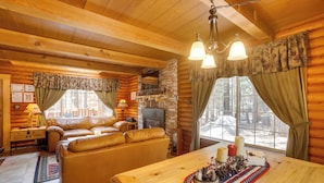 Un accogliente interno di una baita in legno con camino, divano in pelle, tavolo da pranzo in legno e ampie finestre.