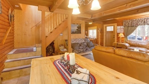 Accogliente interno di una baita in legno con una scala in legno, un divano e un tavolo da pranzo con candele.